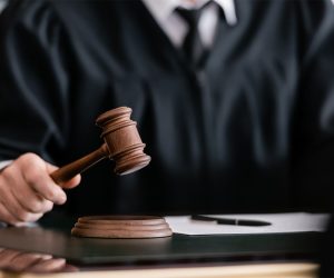 partial view of blurred judge in robe holding gavel in court